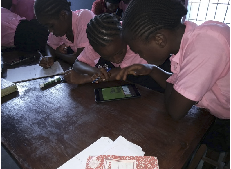 IBT students in pink uniforms collaborating on a tablet